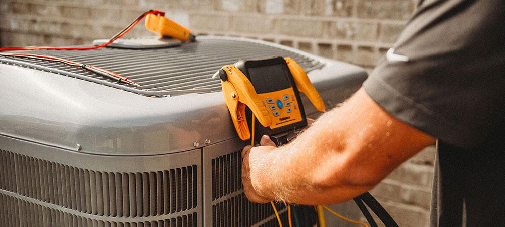 An HVAC technician repairing an outdoor AC unit with tools from a toolbox for Taylor & Tyler HVAC, New Orleans, LA.