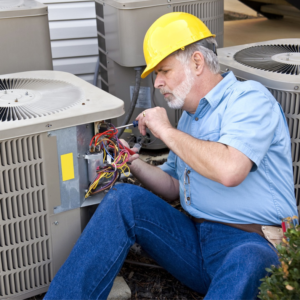 An HVAC technician in a yellow hard hat repairing an outdoor air conditioning unit for Glenn Lima Inc. Heating & Air Conditioning in Wilmington, DE.