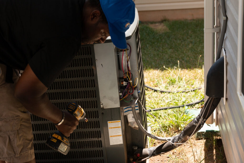 An HVAC technician from Nashville Solutions repairing an outdoor air conditioning unit with a drill in Nashville, TN