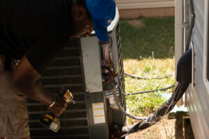 An HVAC technician from Nashville Solutions repairing an outdoor air conditioning unit with a drill in Nashville, TN