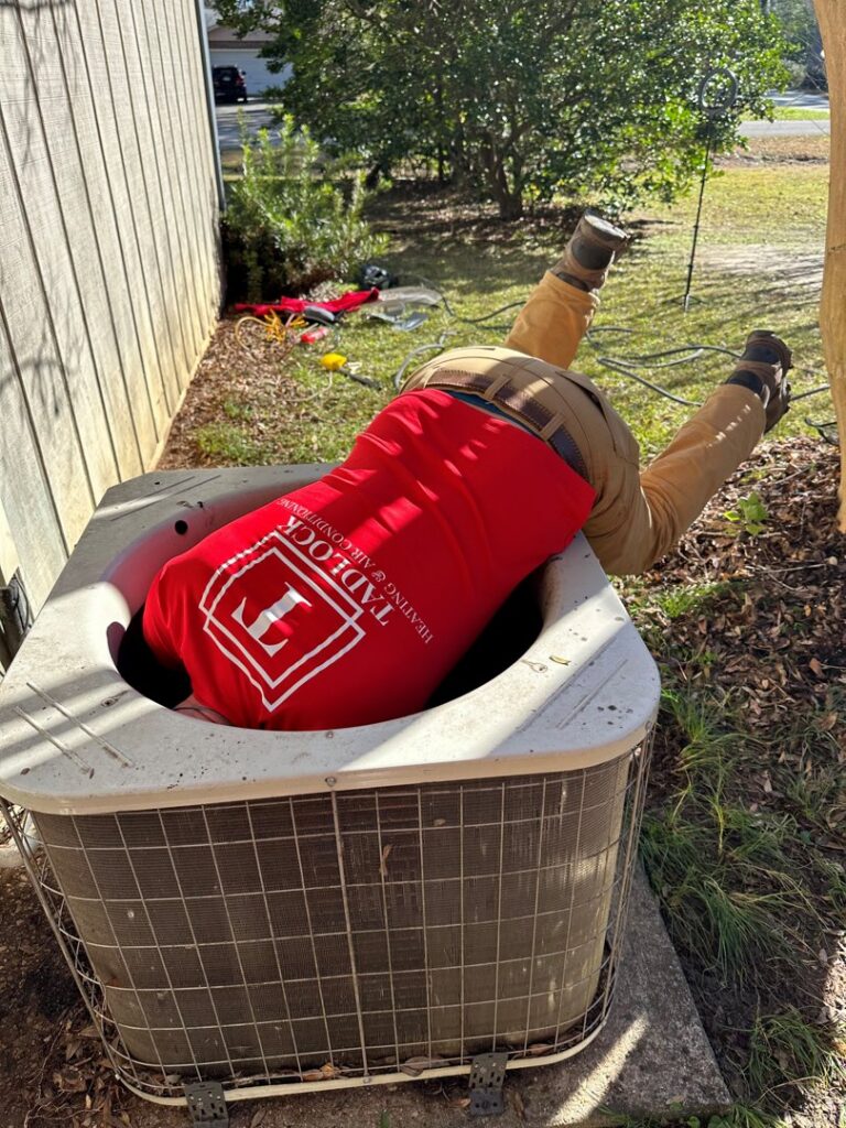 An HVAC technician from Tadlock Heating & Air Conditioning repairing an outdoor unit in Tallahassee, FL