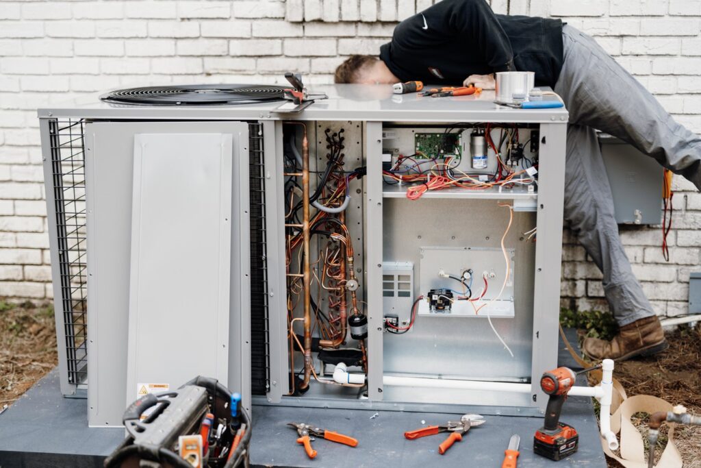 An HVAC technician performing repairs on an open outdoor air conditioning unit for Wingman Heating + Cooling in Auburn, AL.