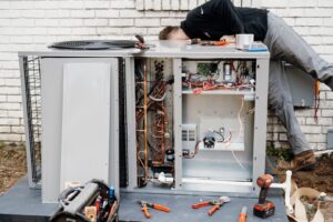 An HVAC technician performing repairs on an open outdoor air conditioning unit for Wingman Heating + Cooling in Auburn, AL.