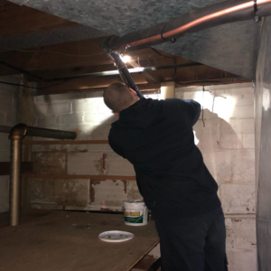 An HVAC technician repairing pipes and ductwork in a basement for SFC Heating and A/C, LLC in Alexandria, VA.