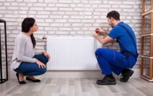 An HVAC technician repairing a radiator while a customer watches at Baker Heating & Cooling in Dayton, OH.