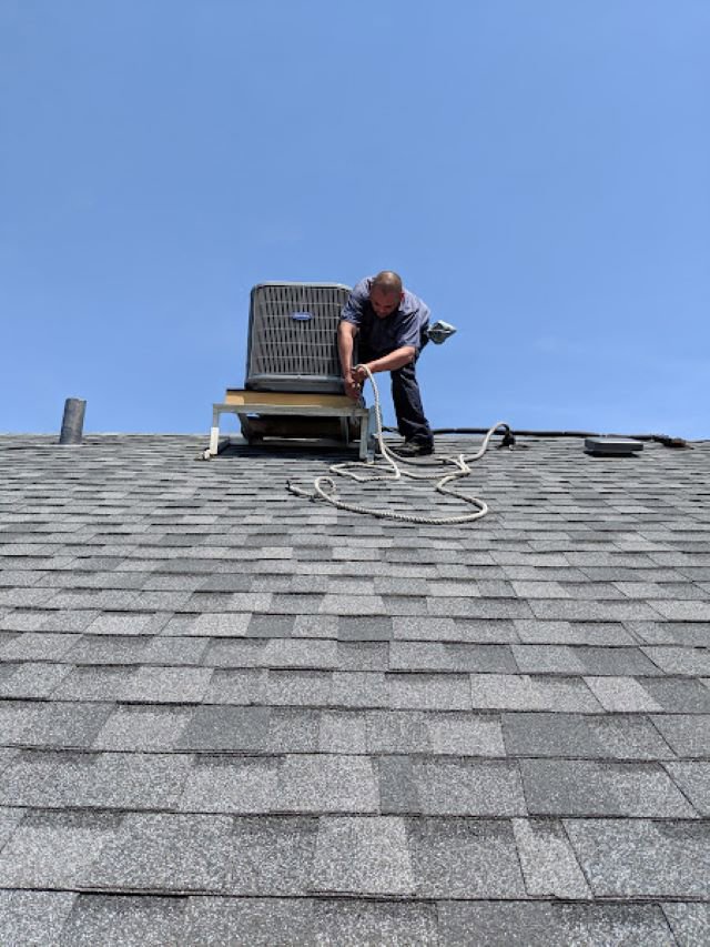 An HVAC technician from Deljo Heating, Cooling & Plumbing repairing a residential rooftop AC unit in Chicago, IL.