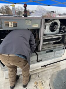 An HVAC technician working inside a large commercial rooftop HVAC unit, performing repairs for Radiant Heating & Cooling in Fishers, IN.