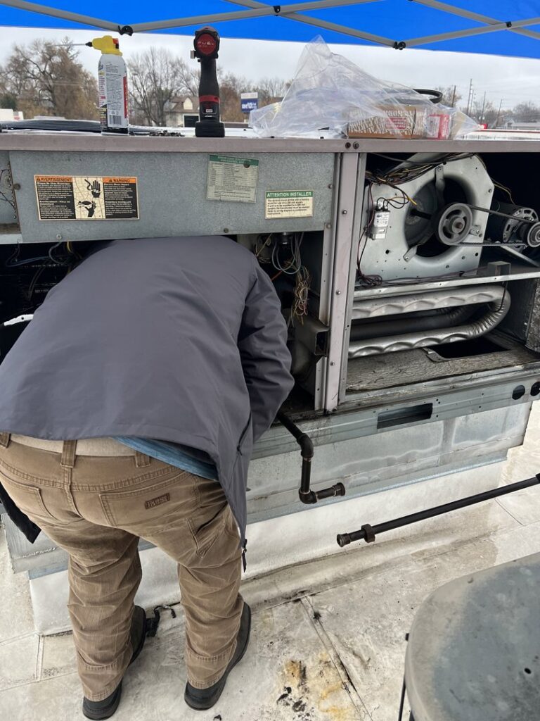 An HVAC technician working inside a large commercial rooftop HVAC unit, performing repairs for Radiant Heating & Cooling in Fishers, IN.