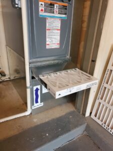 An HVAC technician replacing an air filter in a furnace unit for AccuMax Incorporated in Aurora, IL.