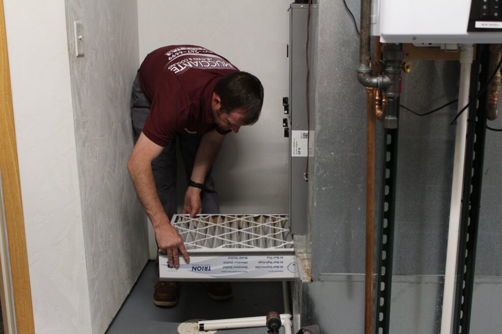 A Mucciante Heating & Cooling technician replacing an air filter in a furnace unit during maintenance in Pekin, IL.