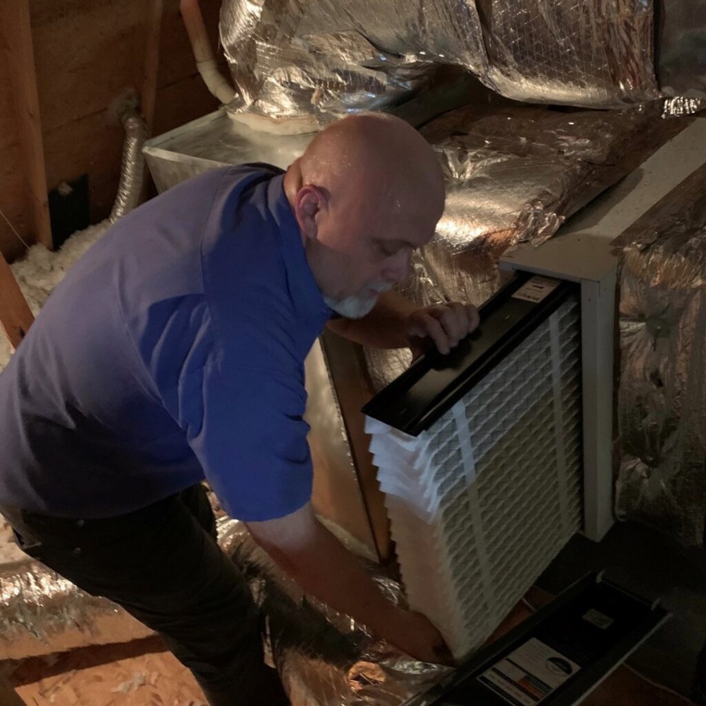 An HVAC technician replacing an air filter in an attic unit, performed by Ward Mechanical Contractors in Denham Springs, LA.