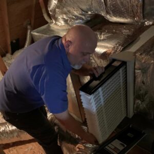 An HVAC technician replacing an air filter in an attic unit, performed by Ward Mechanical Contractors in Denham Springs, LA.
