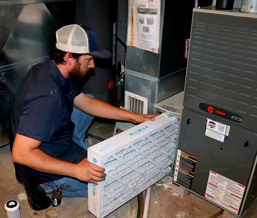 An HVAC technician replacing a furnace filter during a service call for Stoker Mechanical Heating & Air Conditioning in Lawrence, KS.