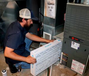 An HVAC technician replacing a furnace filter during a service call for Stoker Mechanical Heating & Air Conditioning in Lawrence, KS.