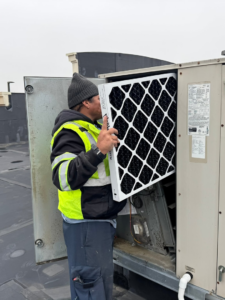 An HVAC technician replacing an air filter in a commercial rooftop unit, performed by GUS' HVAC Services in Canton, GA.