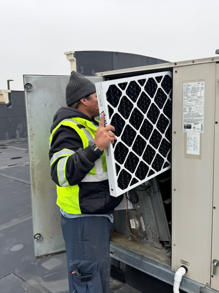 An HVAC technician replacing an air filter in a commercial rooftop unit, performed by GUS' HVAC Services in Canton, GA.
