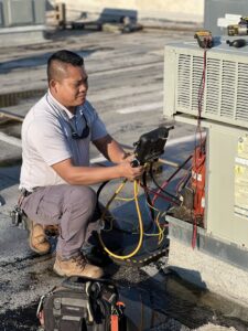 An HVAC technician performing repair and maintenance on a rooftop AC unit for OKIE Heating and Cooling in Tulsa, OK.