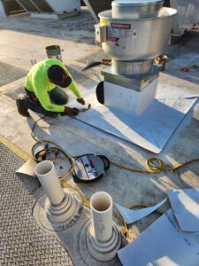 An HVAC technician installing or repairing a rooftop exhaust fan for OKIE Heating and Cooling in Tulsa, OK.