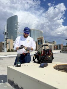 An Instant Air HVAC technician performing service on a rooftop unit with the Las Vegas skyline in the background.