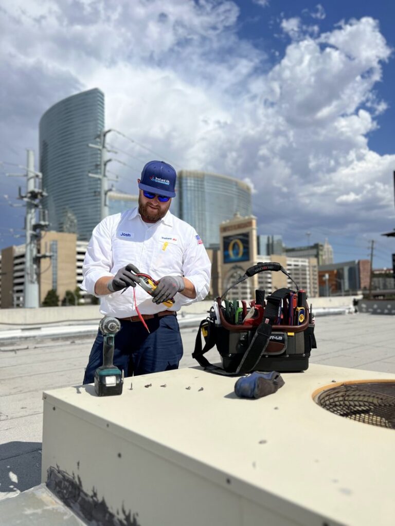 An Instant Air HVAC technician performing service on a rooftop unit with the Las Vegas skyline in the background.