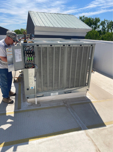 An HVAC technician performing maintenance on a commercial rooftop unit for CHAMPS Heating&Air in Denver, CO