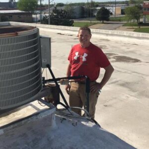 A Pro-Cool Air Conditioning & Heating technician standing next to a commercial rooftop HVAC unit in Blue Springs, MO.