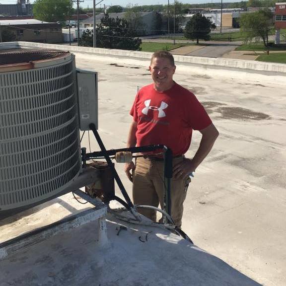 A Pro-Cool Air Conditioning & Heating technician standing next to a commercial rooftop HVAC unit in Blue Springs, MO.