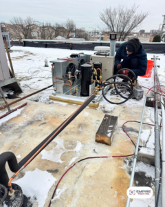 An Empire Tech, Inc. HVAC technician performing repairs on a rooftop unit in snowy conditions in Schaumburg, IL.