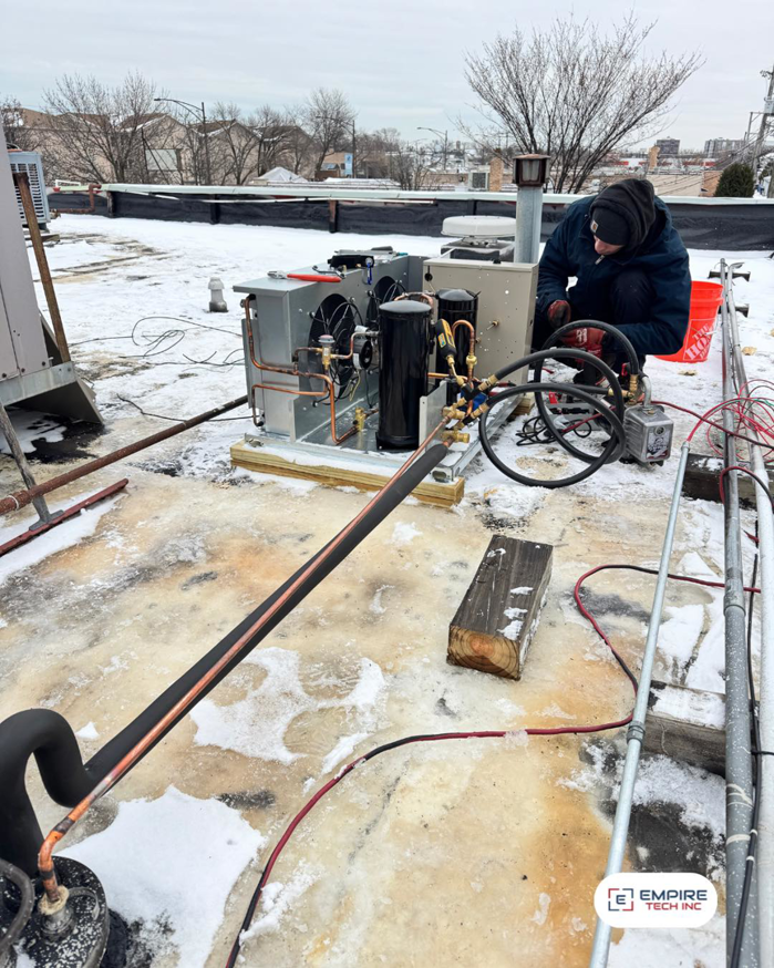 An Empire Tech, Inc. HVAC technician performing repairs on a rooftop unit in snowy conditions in Schaumburg, IL.