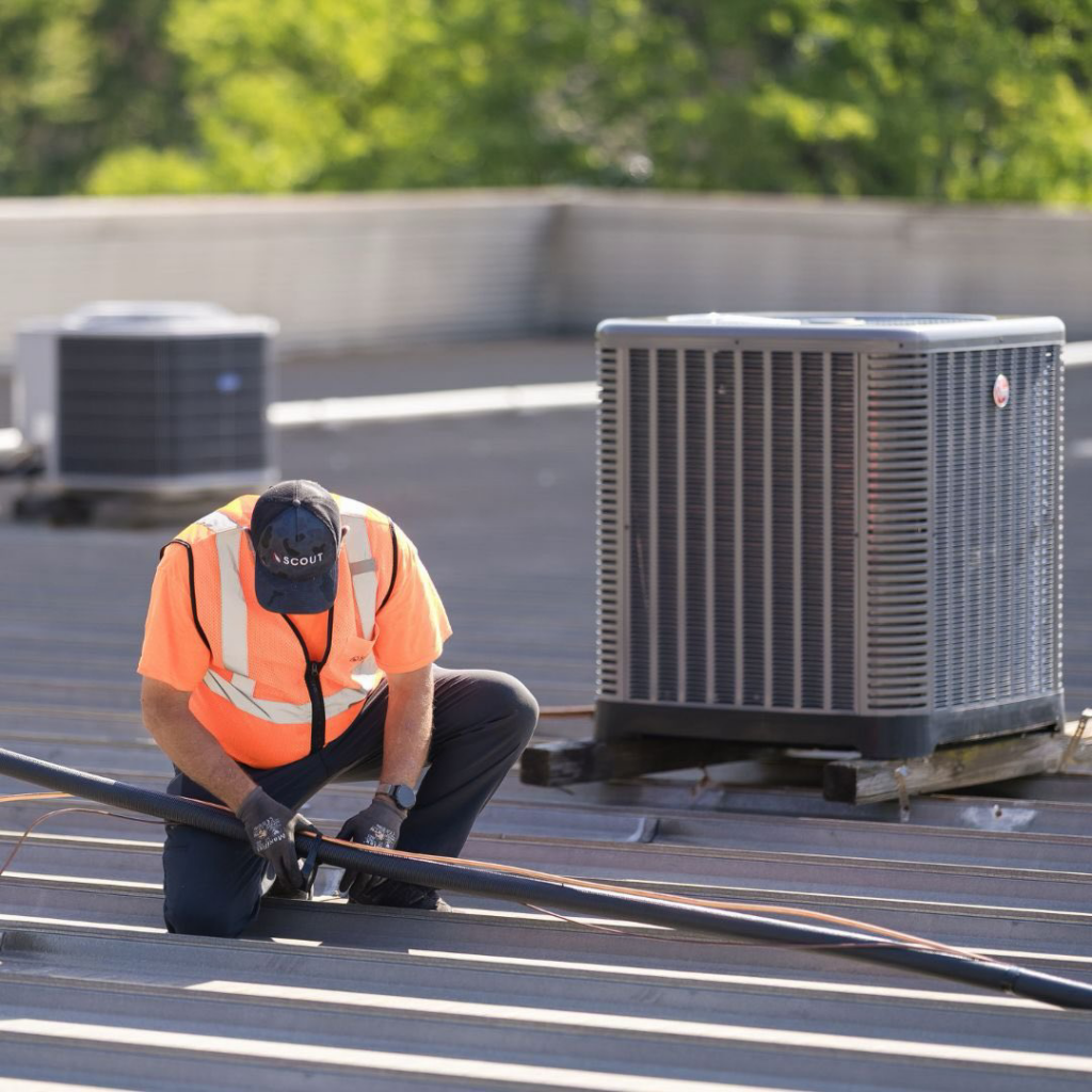 An HVAC technician performing maintenance on a rooftop condenser unit for Scout Mechanical in Greenville, SC.