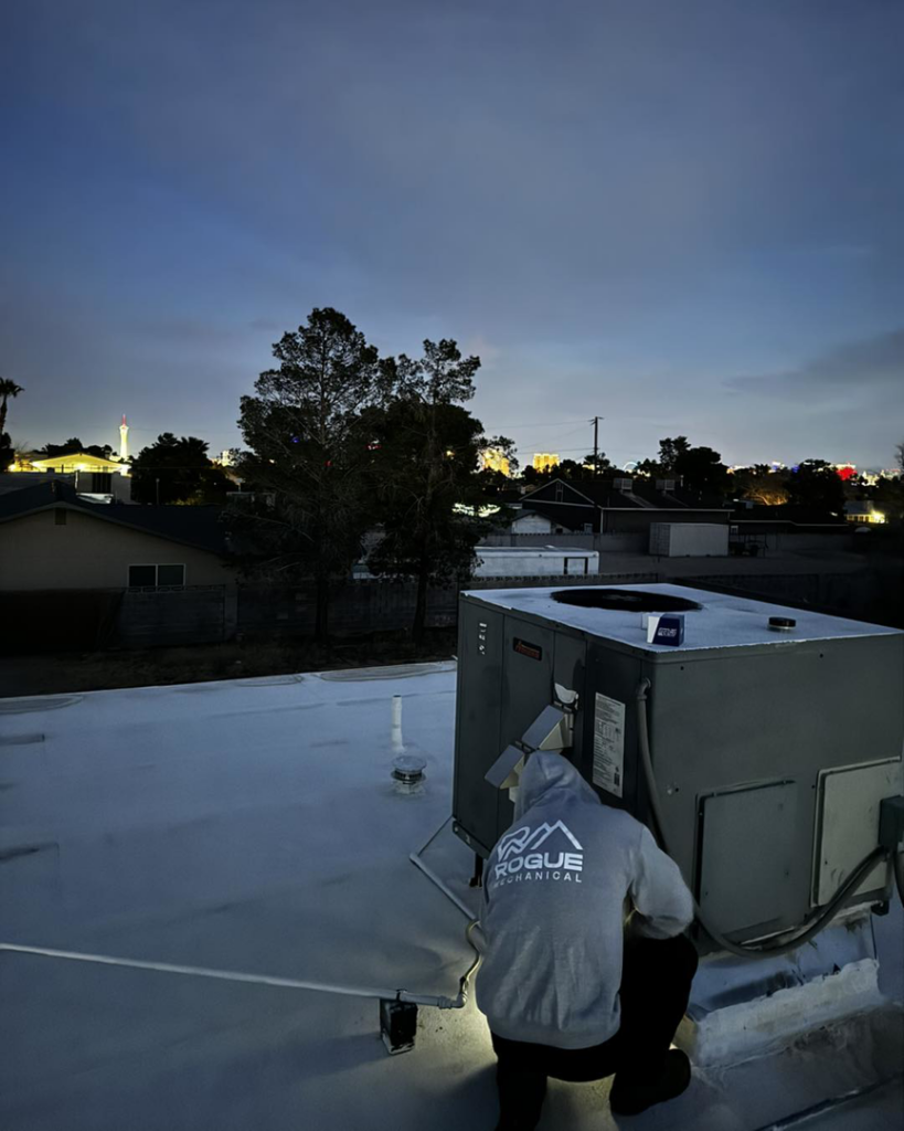 An HVAC technician from Rogue Mechanical working on a rooftop unit at dusk in Las Vegas, NV.