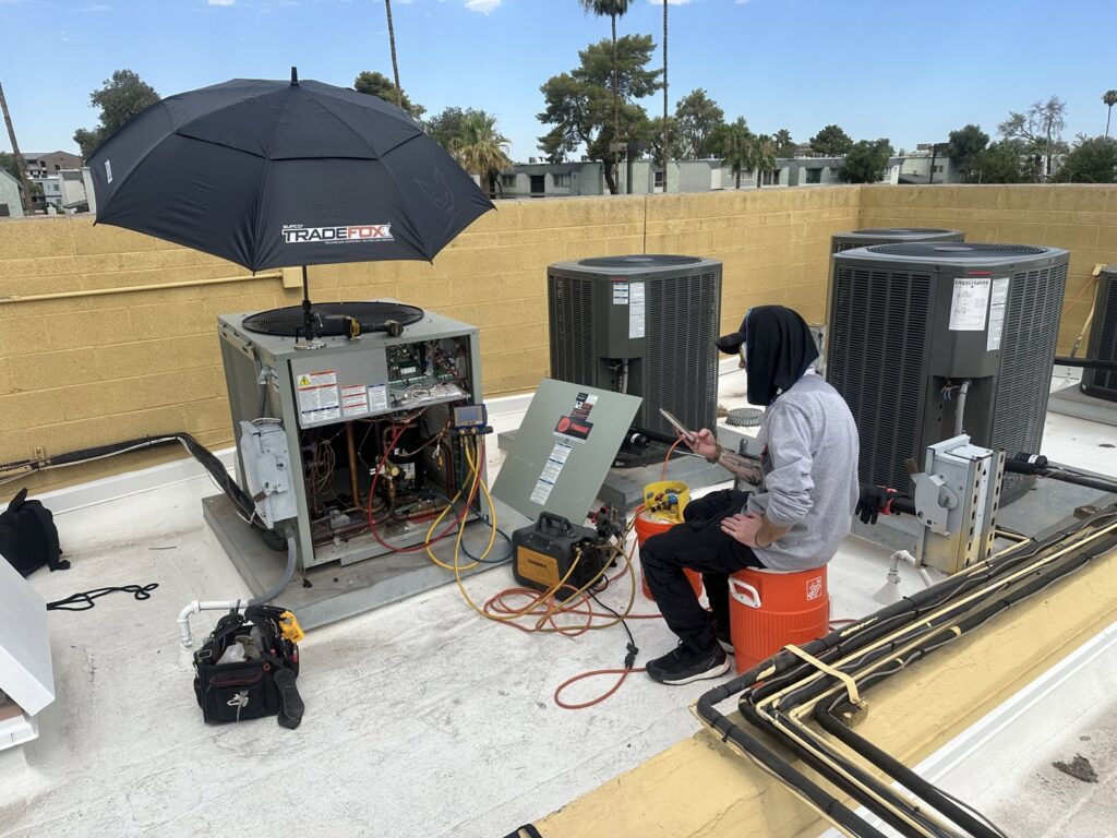 An HVAC technician servicing a rooftop unit with tools and gauges for Gotham Air LLC in Glendale, AZ.