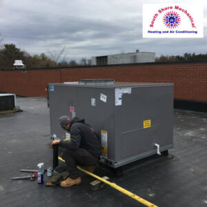 An HVAC technician performing service on a commercial rooftop unit for South Shore Mechanical in Abington, MA