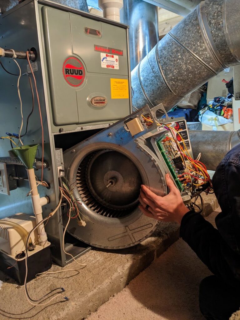 An HVAC technician repairing the blower motor of a Ruud furnace for Reliable Heating & Cooling LLC in Colorado Springs, CO