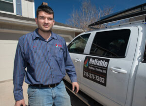 An HVAC technician standing next to a Reliable Heating & Cooling LLC service truck in Colorado Springs, CO