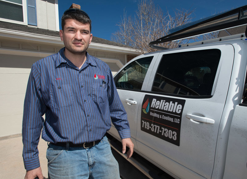 An HVAC technician standing next to a Reliable Heating & Cooling LLC service truck in Colorado Springs, CO
