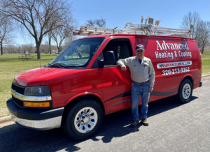 An HVAC technician standing proudly next to a red Advanced Heating & Cooling service van in St. Cloud, MN.