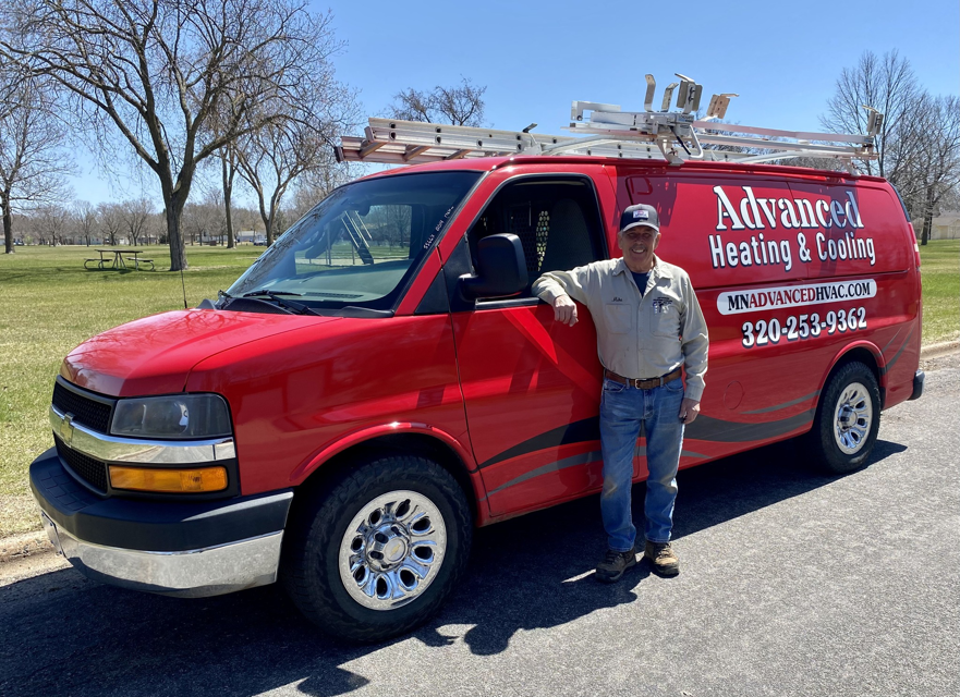 An HVAC technician standing proudly next to a red Advanced Heating & Cooling service van in St. Cloud, MN.