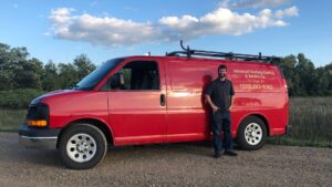 An HVAC technician standing next to an Advanced Heating & Cooling service van in a field in St. Cloud, MN.