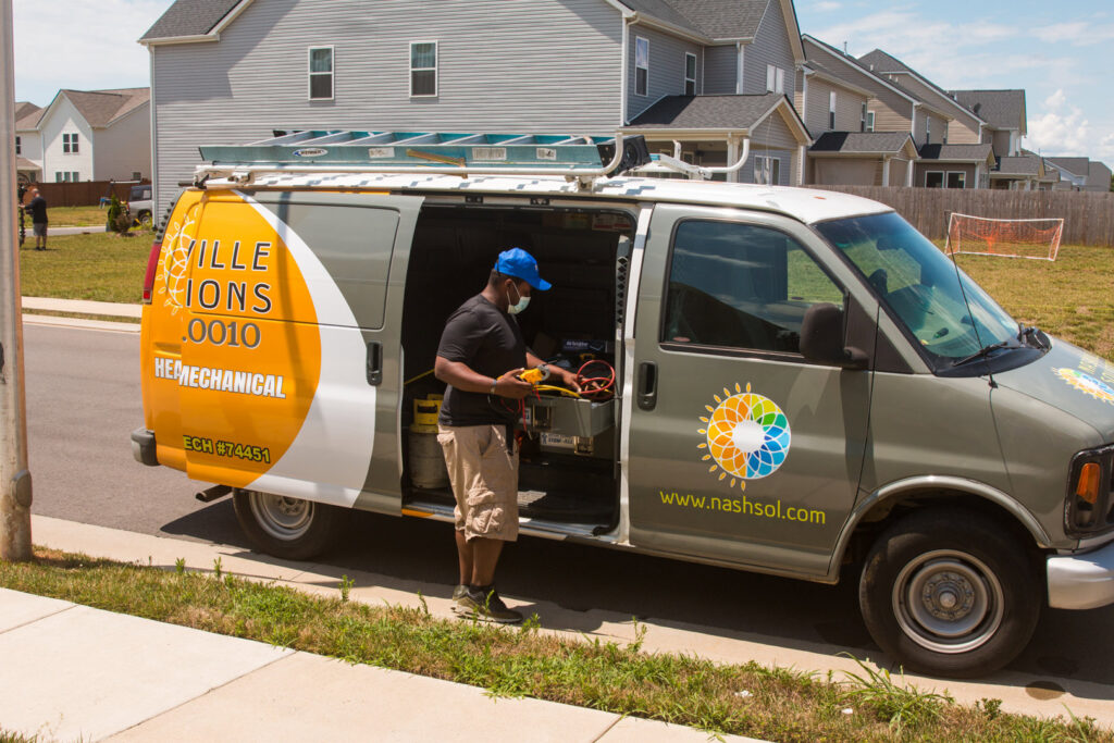 An HVAC technician from Nashville Solutions preparing for a job next to a branded service van in Nashville, TN