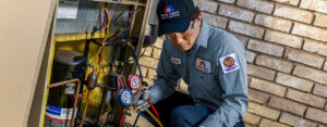 An HVAC technician from Chief/Bauer Service Experts servicing an AC compressor unit with gauges in Champaign, IL.
