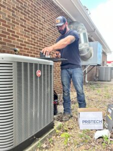 An HVAC technician servicing an outdoor AC condenser unit for Anderson's Air in Newport News, VA