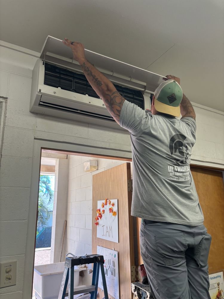 An Ultimate Air Conditioning technician opening an indoor AC unit for maintenance or repair in Pearl City, HI