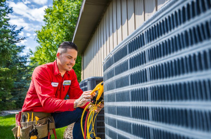 An Advanced Home Services technician performing maintenance on an outdoor AC condenser unit in Rigby, ID.