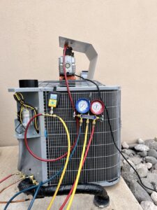 An HVAC technician servicing an outdoor AC unit with gauges connected by Aircon Heating and Cooling Inc in Las Cruces, NM