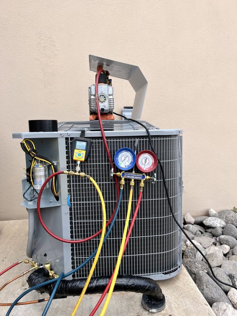 An HVAC technician servicing an outdoor AC unit with gauges connected by Aircon Heating and Cooling Inc in Las Cruces, NM