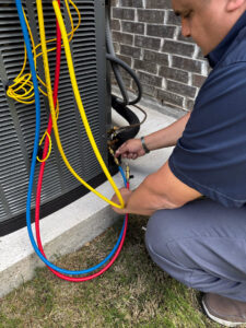An HVAC technician from Climate Control servicing an outdoor air conditioning unit with gauges in San Antonio, TX