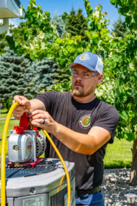 An HVAC technician from Comfort Craftsman Heating & Cooling servicing an outdoor AC unit in Westland, MI.