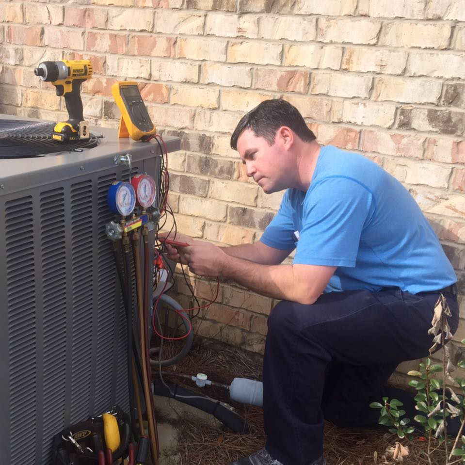 An HVAC technician from Comfort Pros servicing an outdoor air conditioning condenser unit with gauges in Mobile, AL.