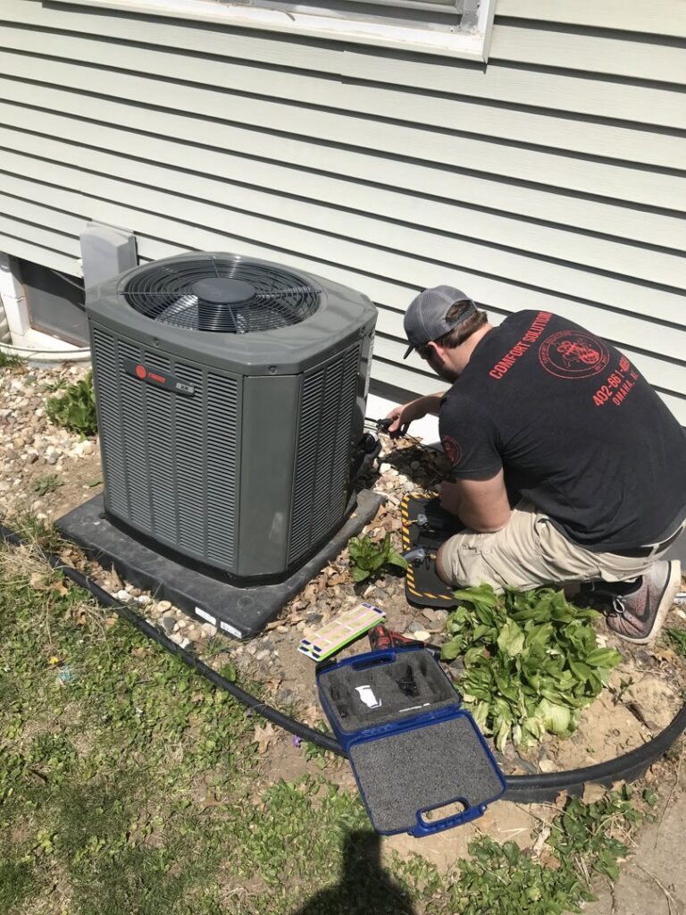 An HVAC technician from Comfort Solutions Heating and Air Conditioning servicing an outdoor AC unit in Omaha, NE.